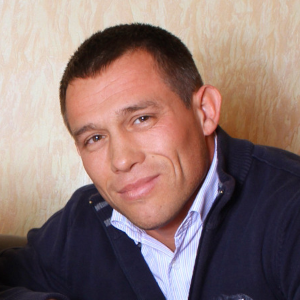 Мужчина который кушал суши он с короткими темными волосами в темно-синем свитере и рубашке, который улыбается на нейтральном фоне.